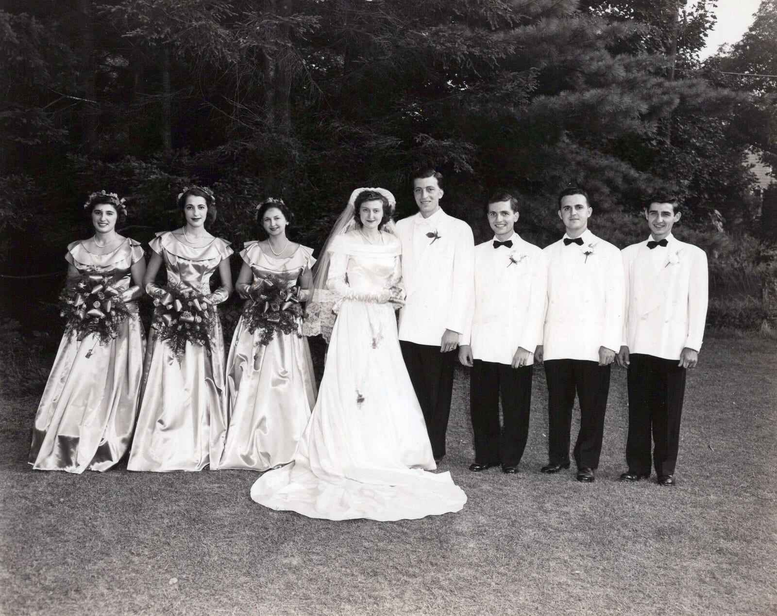 A 1948 wedding party on a lawn: four bridesmaids, the bride, and four men in white dinner jackets